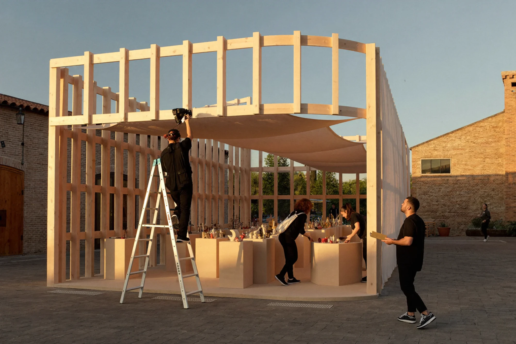 A team installs a wooden pavilion for a brand experience at golden hour.