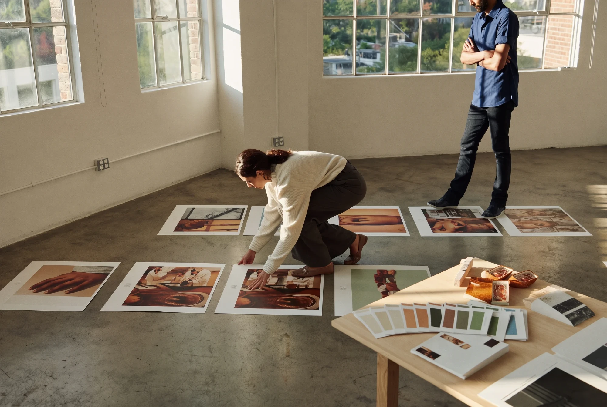 Two people reviewing large photo prints laid out on a studio floor.