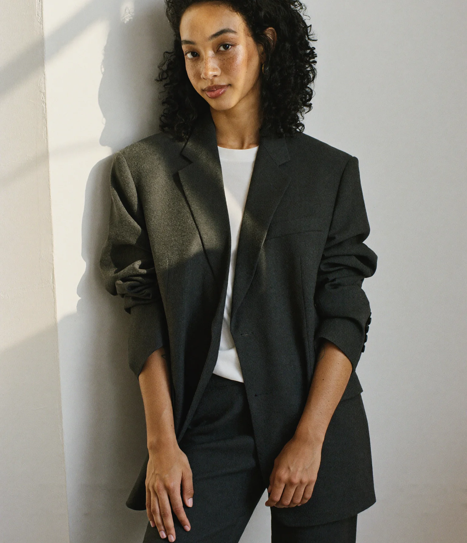 Illustrative editorial portrait of a person in a charcoal blazer.